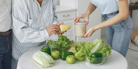 Starsza pani z pomocą młodej kobiety przygotowuje posiłek. Na stole warzywa i płatki – kluczowe dla diety w chorobie Parkinsona.