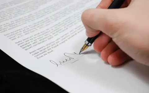 Dłoń podpisuje dokument piórem. Zastanawiasz się, jakie składki płaci emeryt od umowy zlecenia?