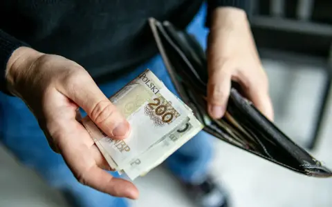 Dłonie trzymają banknoty 200 zł i pusty portfel. Może to symbolizować trudności finansowe i potrzebę wsparcia z opieki społecznej.