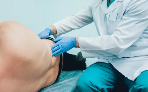 Lekarz od pęcherza w niebieskich rękawiczkach bada pacjenta leżącego na kozetce.