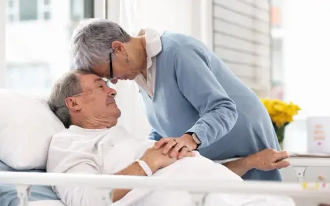 Czule pożegnanie. Kobieta pochyla się nad umierającym mężem, jak poznać że chory na alzheimera umiera, widać troskę i miłość.