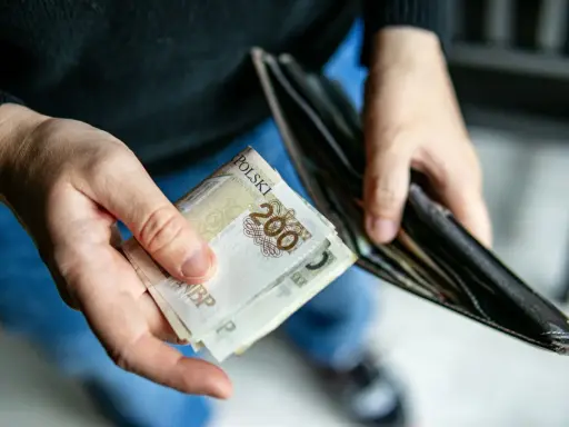 Dłonie trzymają banknoty 200 zł i pusty portfel. Może to symbolizować trudności finansowe i potrzebę wsparcia z opieki społecznej.