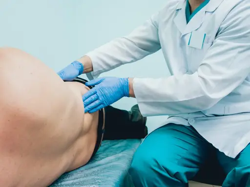 Lekarz od pęcherza w niebieskich rękawiczkach bada pacjenta leżącego na kozetce.