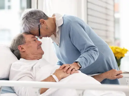 Czule pożegnanie. Kobieta pochyla się nad umierającym mężem, jak poznać że chory na alzheimera umiera, widać troskę i miłość.