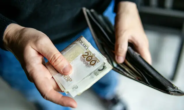 Dłonie trzymają banknoty 200 zł i pusty portfel. Może to symbolizować trudności finansowe i potrzebę wsparcia z opieki społecznej.