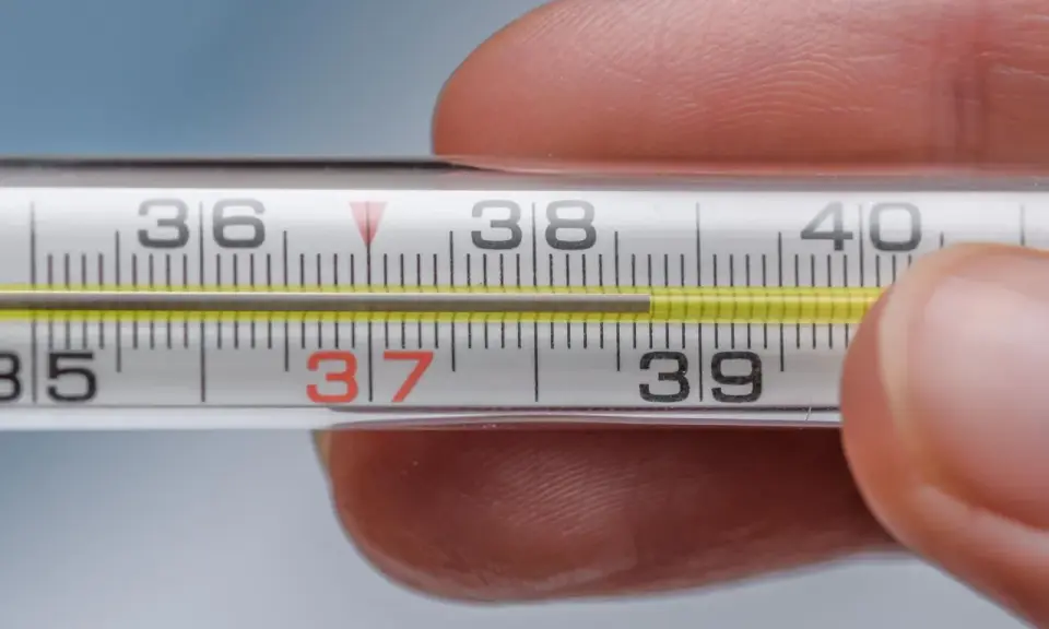 Zbliżenie na termometr rtęciowy, gdzie słupek rtęci wskazuje 37.1 temperatura. Dłoń trzyma termometr.