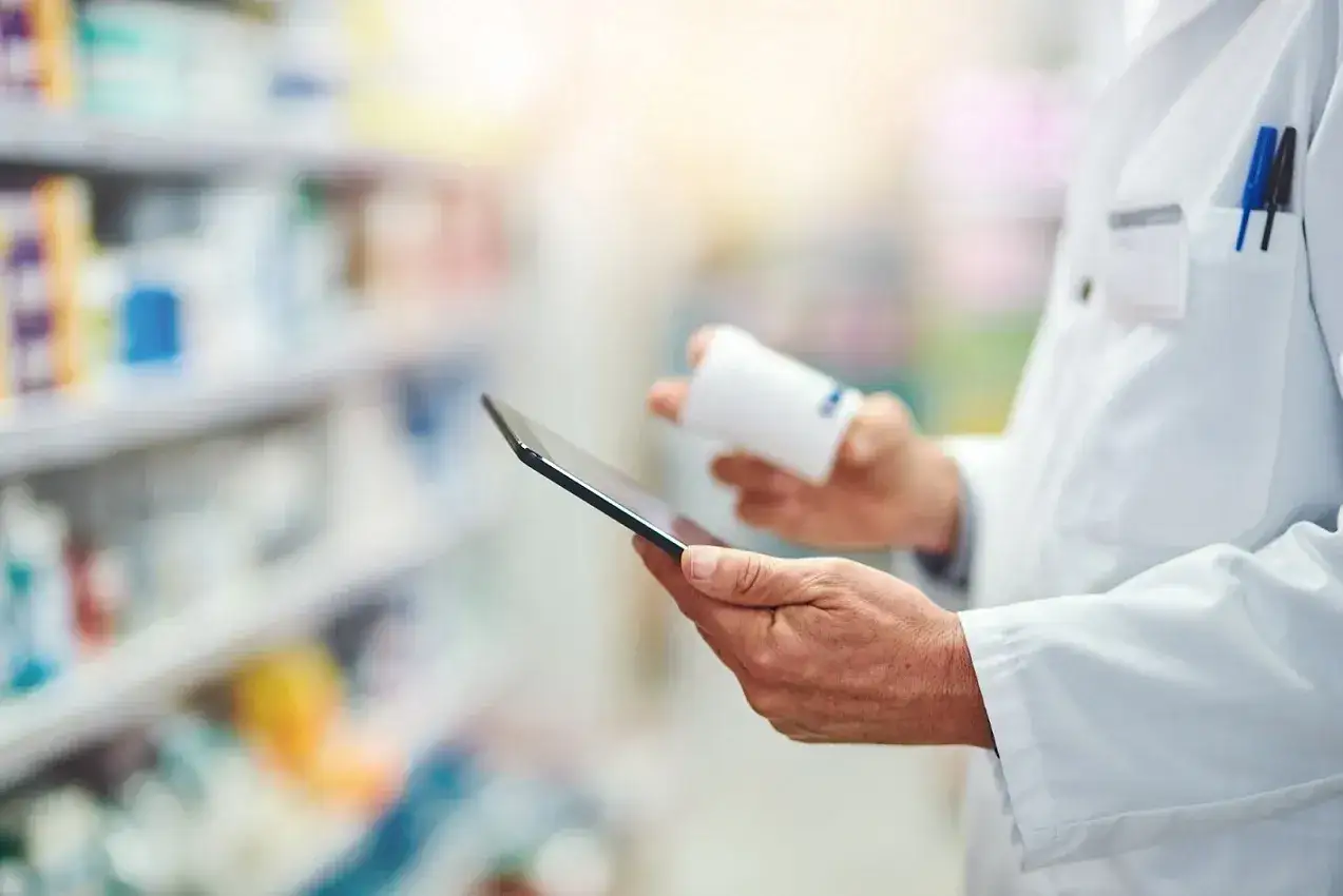 Farmaceuta sprawdza receptę na tablecie, przygotowując zwrot za leki dla seniorów.