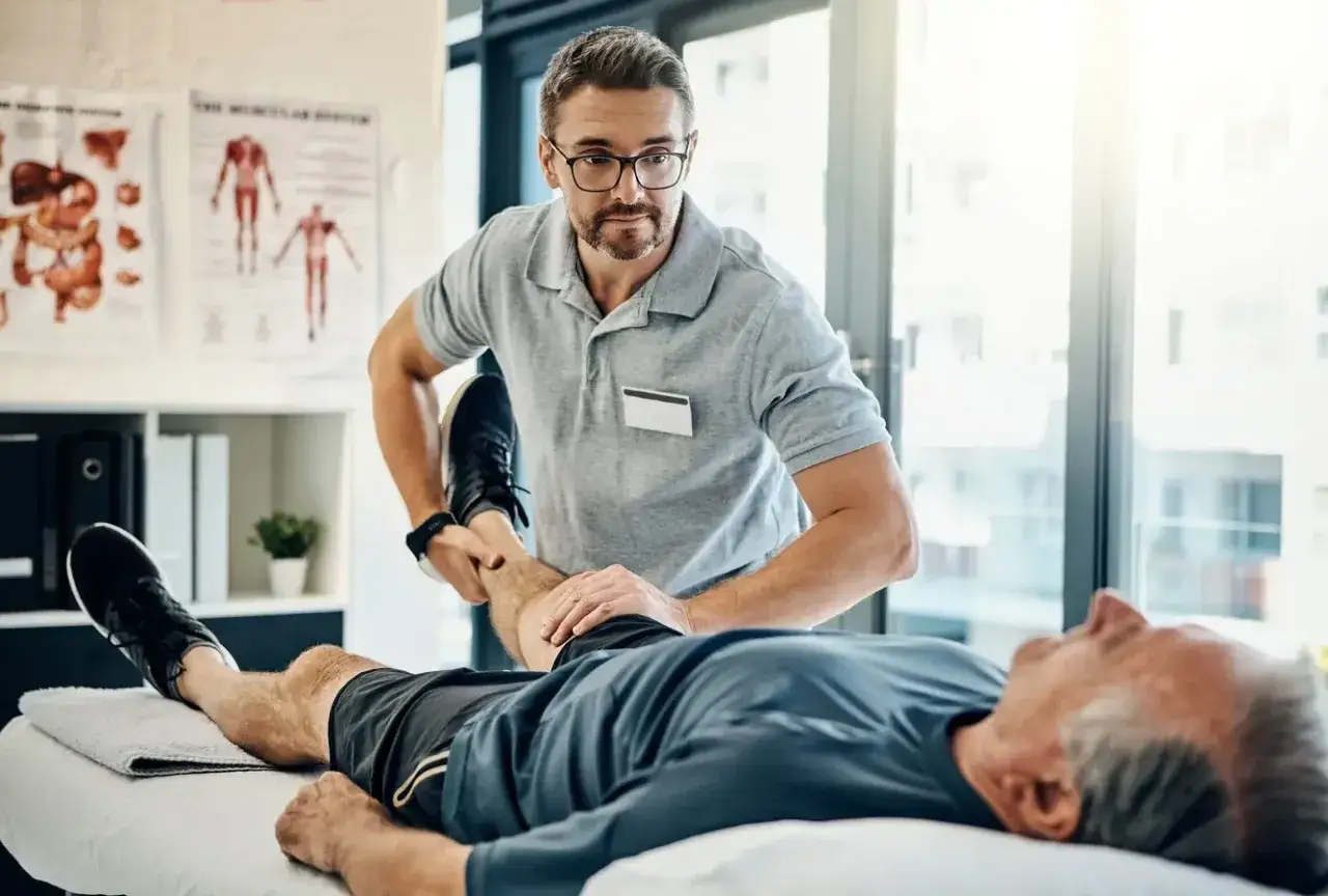 Fizjoterapeuta ćwiczy nogę starszego pacjenta. Dowiadujemy się, komu przysługuje szpital uzdrowiskowy.