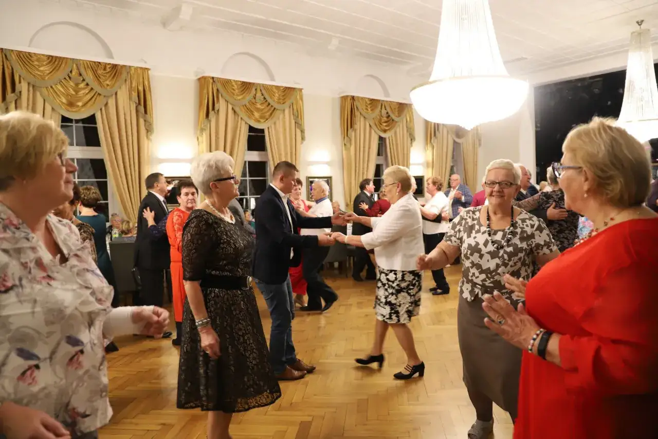 Uczestnicy wieczork&oacute;w zapoznawczych dla senior&oacute;w tańczą w eleganckiej sali.