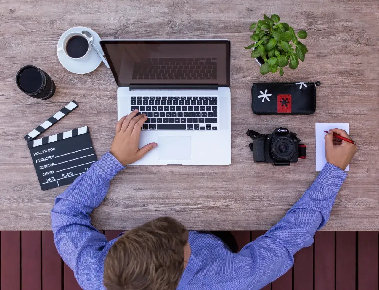Emeryt pracuje w domu nad projektem filmowym. Na biurku laptop, aparat, klaps i kawa. Idealna praca dla emeryta w domu.