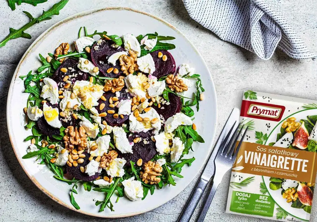 Sałatka z burakiem i kozim serem, rukolą, orzechami i nasionami. Obok opakowanie sosu Vinaigrette Prymat.